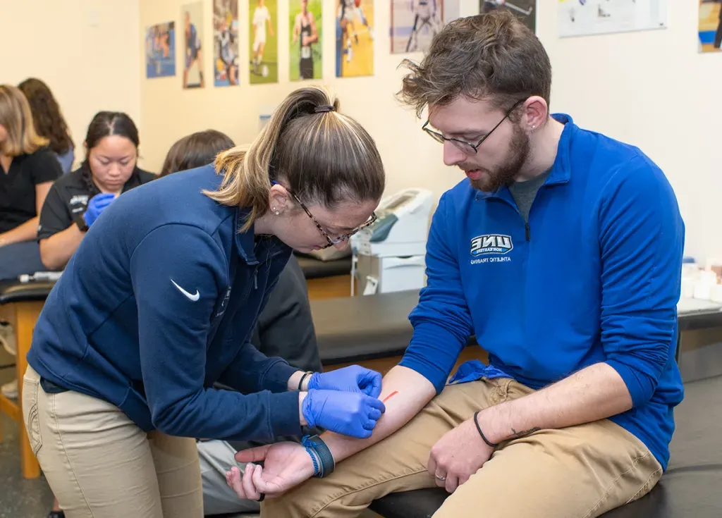 An athletic training student practices mending a wound on another A.T. student 